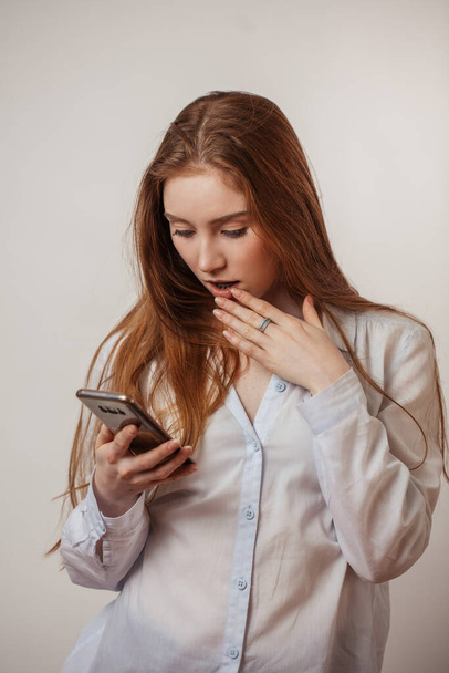 Young emotional attractive redhead female holding smartphone iso - Foto, afbeelding
