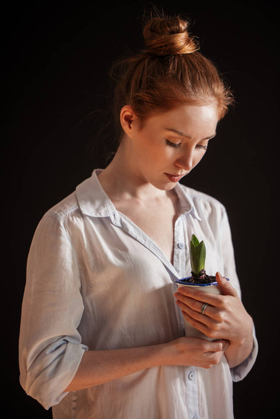 Ginger young girl holding potted plant isolated over black backg - Foto, Imagen
