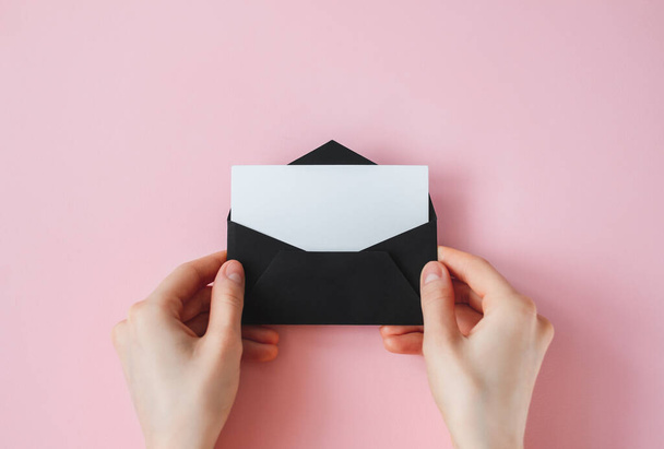 Black envelope with white blank paper in female hands on a pink background. High quality photo - Zdjęcie, obraz