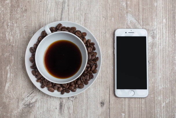 Tasse Kaffee mit Kaffeebohnen herum und einem Telefon auf einem alten hölzernen Hintergrund - Foto, Bild