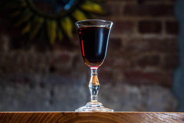 Dark red tincture or liqueur in a glass is on the table in the night bar - Foto, imagen