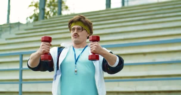 Funny Caucasian retro style fitness trainer having workout outdoors near stairs. Handsome vintage man with mustache in glasses doing exercise with dumbbells on street. Sport lifestyle. 60s concept - Footage, Video