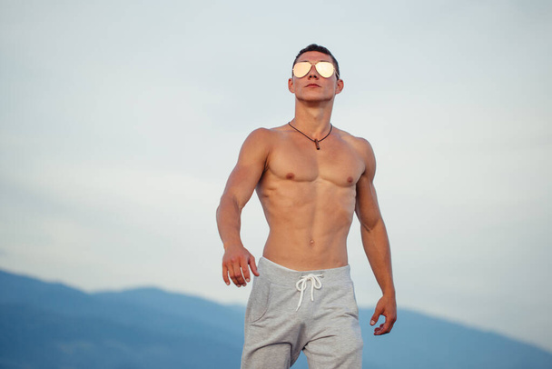 Masculine body man in sunglasses at beach with mountauns on background - Valokuva, kuva
