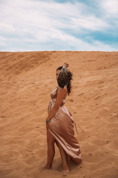 Dark girl with voluminous curly hair among the Sands in the sand dune. Beautiful woman in the desert - Photo, image