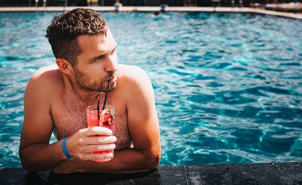 若い熱い男が水溜まりで休んでいる。水の中の男の写真エッジに傾き、カクテルを飲む。男は右に見える。夏休みには水の中で一人で時間を過ごす。リゾートスパの場所. - 写真・画像