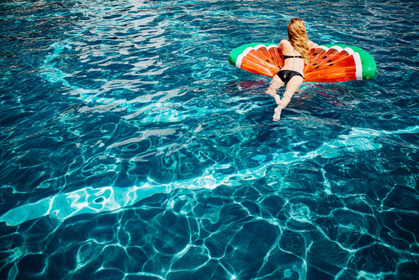 Młoda, gorąca kobieta odpoczywająca w basenie. Widok z tyłu zdjęcie zrelaksowanej szczupłej kobiety w czarnym stroju kąpielowym leżącej na pierścieniu pływackim w wodzie i bawiącej się. Kobieta kąpiel samotnie w ośrodku spa miejsce w lecie. - Zdjęcie, obraz