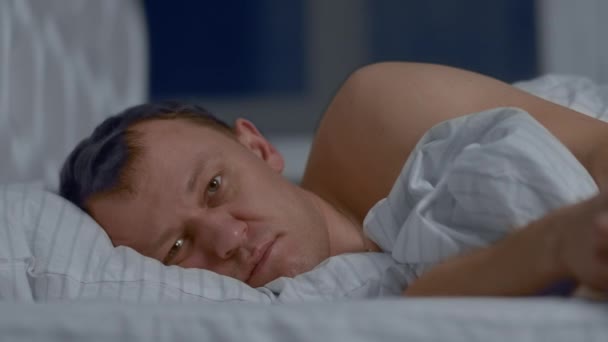 Portrait of a man cannot fall asleep lies on the bed with wide open eyes, camera movement, close-up - Filmmaterial, Video