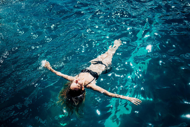 Młoda, gorąca kobieta odpoczywa sama. Zdjęcie spokojnej, zrelaksowanej dziewczyny w wodzie. Patrząc w niebo i opalając się. Ciesz się wakacjami samotnie. - Zdjęcie, obraz