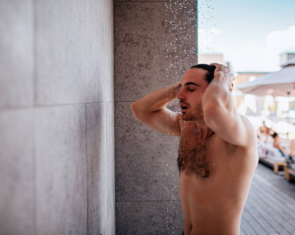 外でシャワーを浴びてる若い男。トップレス強い強力な男の頭と体を洗う。落下する水のプロセスをお楽しみください。リゾートスパで夏休みを過ごす. - 写真・画像