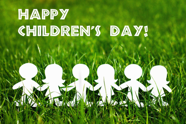 Silhouettes of children holding hands cut out of cardboard on a background of grass. Girls and boys made of white paper. International children's day. Copy space - Photo, image
