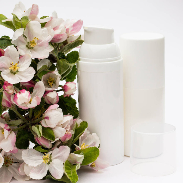Garrafas cosméticas brancas com flores de pêra em um fundo branco. Conceito de cosméticos orgânicos naturais
 - Foto, Imagem