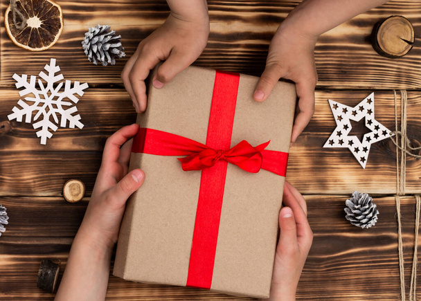 Dłonie dając lub otrzymując prezent w papierze rzemieślniczym z czerwoną wstążką na rustykalnym drewna Boże Narodzenie i Nowy Rok tle. Widok z góry - Zdjęcie, obraz