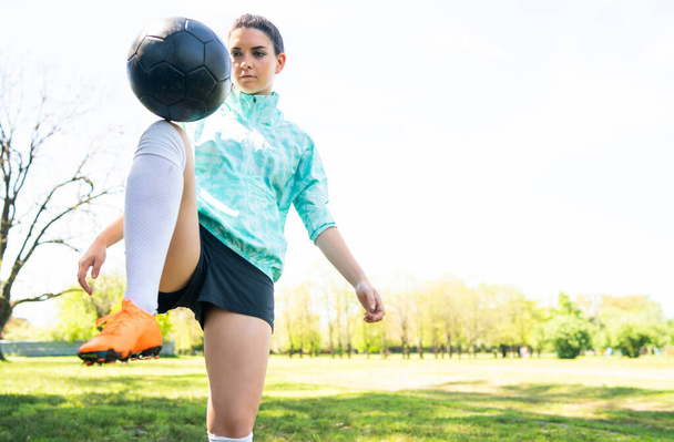 Portrait of young woman practicing soccer skills and doing tricks with the football ball. Soccer player juggling the ball. Sports concept. - 写真・画像