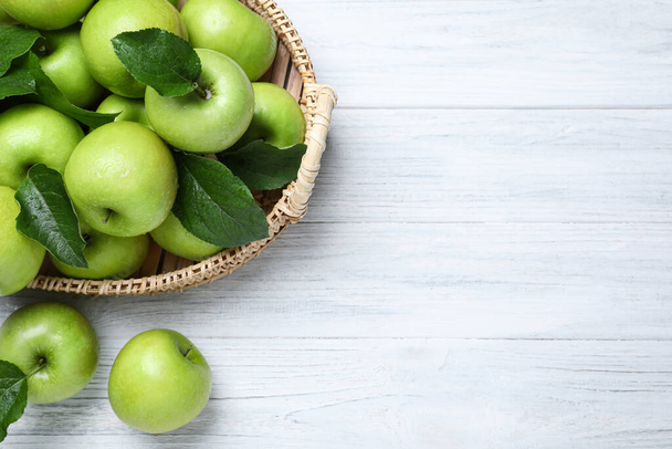 Juicy green apples in wicker tray on white wooden table, flat lay. Space for text - Фото, изображение