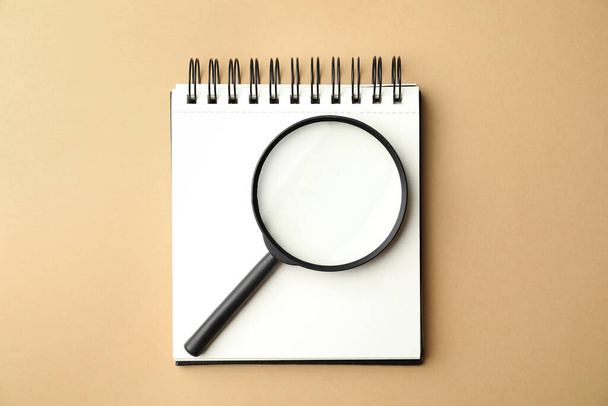 Magnifier glass and empty notebook on beige background, flat lay with space for text. Find keywords concept - Valokuva, kuva
