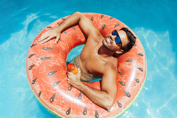 Handsome man relaxing alone on a float in the pool on a hot summer day - Foto, immagini