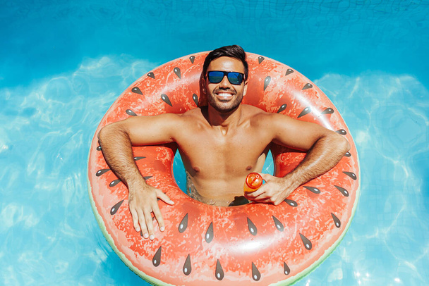 Handsome man relaxing alone on a float in the pool on a hot summer day - Foto, Imagem