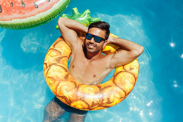Handsome man relaxing alone on a float in the pool on a hot summer day - Fotó, kép