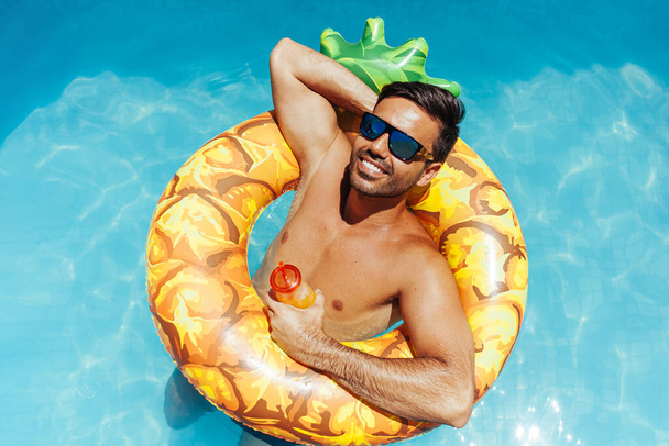 Handsome man relaxing alone on a float in the pool on a hot summer day - Foto, Imagem