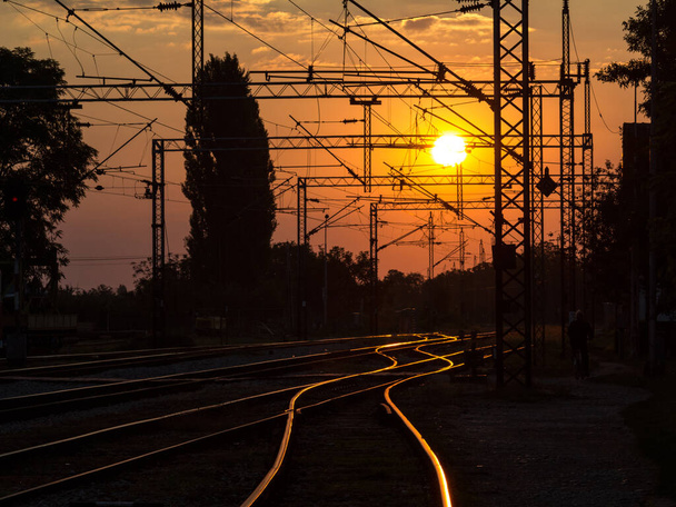 Sırbistan 'ın Sremska Mitrovica kentinde gün batımında demiryolu rayları ve tepe hatları, Balkanlar' da elektrik yüklü bir demiryolu hattının tren istasyonunda - Fotoğraf, Görsel