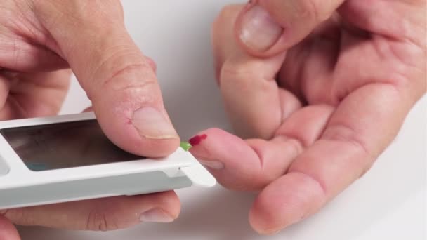proceso de tomar sangre de un dedo a una tira de prueba para determinar el azúcar en la sangre, la mano de un hombre sostiene un glucosímetro electrónico con un monitor, la sangre sale del dedo, primer plano
 - Metraje, vídeo