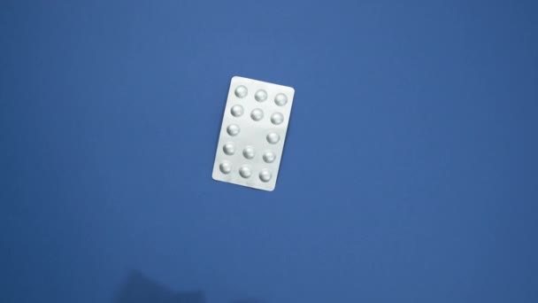 Comprimidos redondos en un blíster, dos manos femeninas colocan medicamentos sobre un fondo azul, vista superior - Imágenes, Vídeo