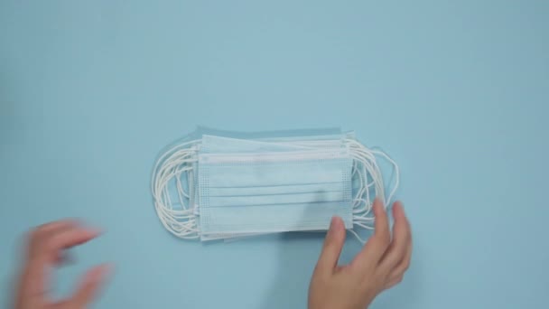 set of disposable medical masks, a pair of latex blue gloves and goggles, female hand folds protective equipment on a blue background, top view - Filmagem, Vídeo