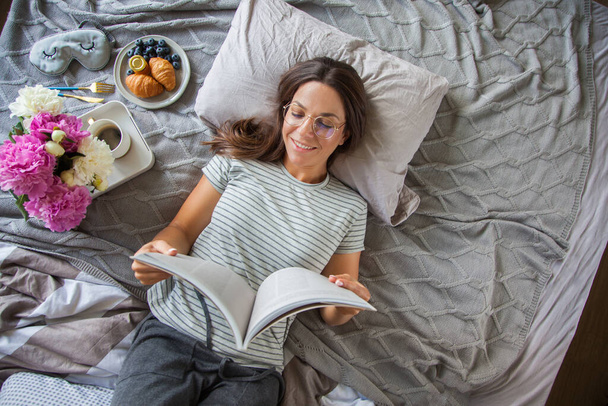 Woman reading book or newspaper and drinking coffee breakfast on bed during the morning - Fotó, kép