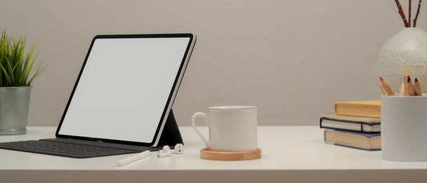 Gesneden shot van blanco tablet op witte tafel met koffiebeker, briefpapier en decoraties - Foto, afbeelding