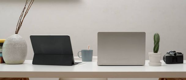 Lähikuva kotitoimiston työpöytä digitaalisilla laitteilla, kamera, muki ja koristeet valkoisella pöydällä  - Valokuva, kuva