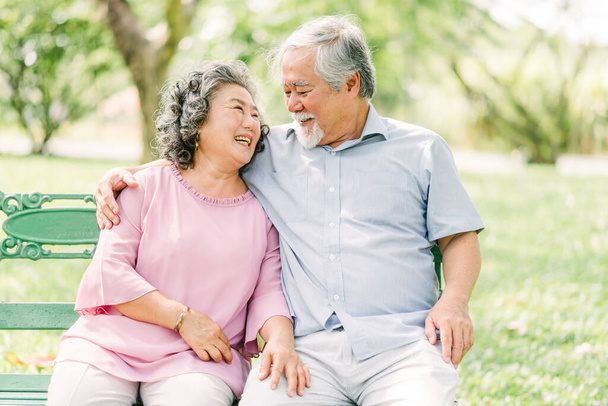 Glückliches asiatisches Seniorenpaar, das eine gute Zeit hat. Sie lachen und lächeln, während sie draußen im Park sitzen - Foto, Bild