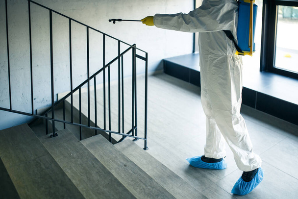 商店街の階段を掃除する作業員を防腐剤で消毒し、コビト19の拡散を防ぎます。消毒服を着た男が階段をスプレーします。医療、隔離、衛生の概念 - 写真・画像