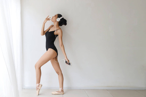 спортивна і здорова молода азіатська жінка з красивим обличчям, що практикує балет зі смартфоном, слухаючи музику з навушників
 - Фото, зображення