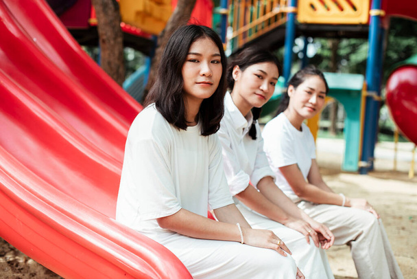Dreifache Zwillingsschwester sitzt am Ende des roten Schiebereglers auf dem Spielplatz und schaut in die Kamera. - Foto, Bild