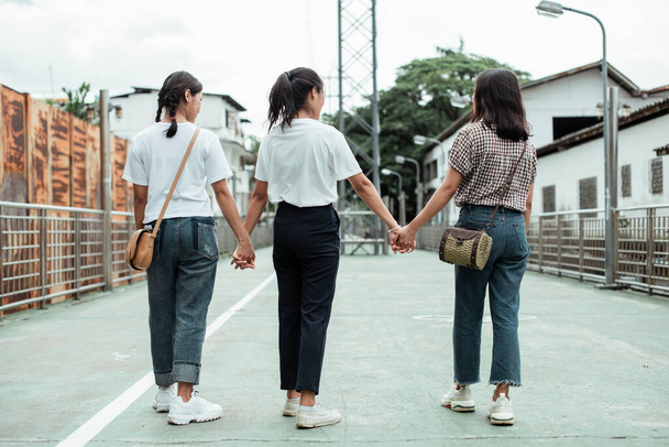 Foto trasera de la hermana gemela triple tomándose de las manos y caminando juntos en la ciudad
. - Foto, imagen