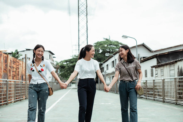 Triple sœur jumelle se tenant la main tout en marchant dans la vieille ville dans la rue. - Photo, image