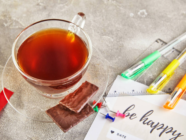 Uma xícara de café com canetas de chocolate e coloridas, folhas de um diário com a inscrição em um fundo de concreto cinza
. - Foto, Imagem