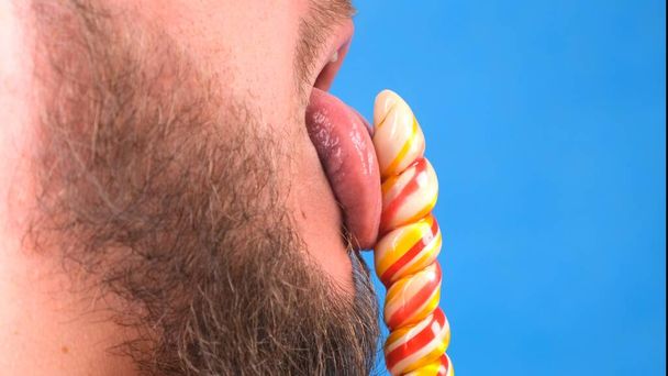 Male sexually licks candy lollipop on a blue background. - Photo, Image