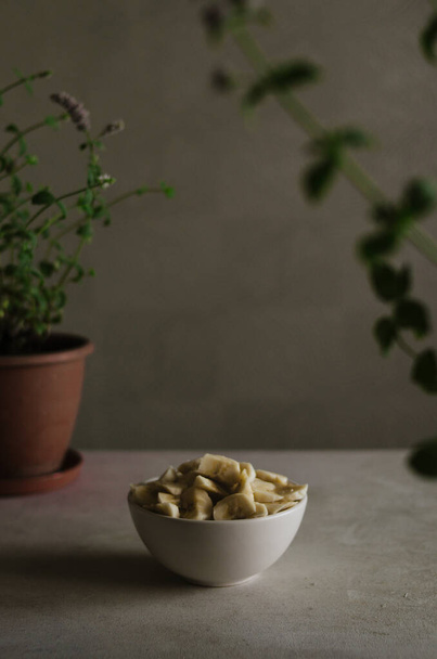 Hübsche kleine Schüssel mit geschnittenen Bananen auf dem Tisch in der Küche mit Minzpflanzen Dekoration. Leckeres und gesundes vegetarisches Essen  - Foto, Bild