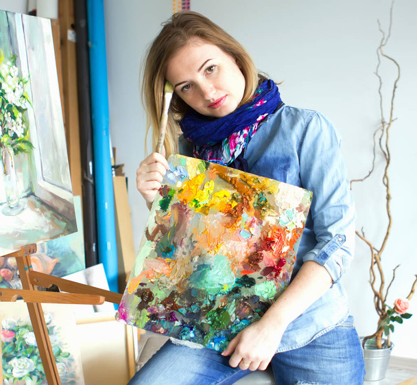 girl artist with a palette of paints in hands. looks directly into the camera. Art studio - Fotografie, Obrázek