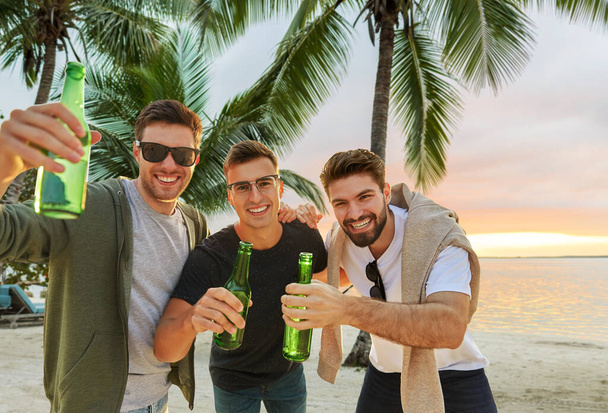 young men toasting non alcoholic beer on beach - Valokuva, kuva