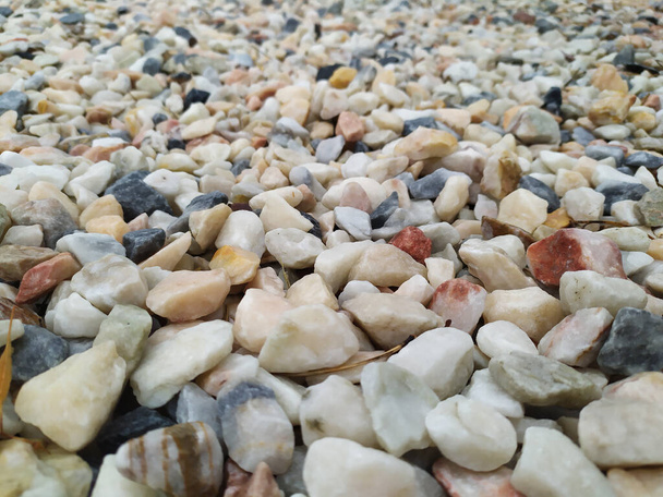 Ακατέργαστα πετρώματα και ορυκτά ως φυσικό πέτρωμα με θρυμματισμένο και ακατέργαστο υλικό σε τραχιά ακτή ή βραχώδη παραλία παρουσιάζουν ψήγματα και ψαμμίτες σε αρμονικά παστέλ χρώματα - Φωτογραφία, εικόνα