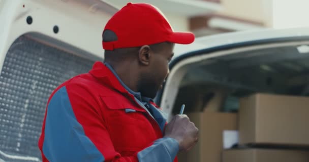 輸送会社の男性アフリカ系アメリカ人労働者は、バンに小包カートンボックスをカウントし、それを書き留めます。閉じろ!. - 映像、動画
