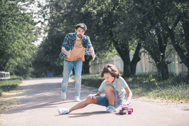 Dark-haired boy falling down on the ground, his dad rushing to help him - 写真・画像