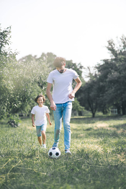 Dark-haired boy and his father playing with the ball in the garden - 写真・画像