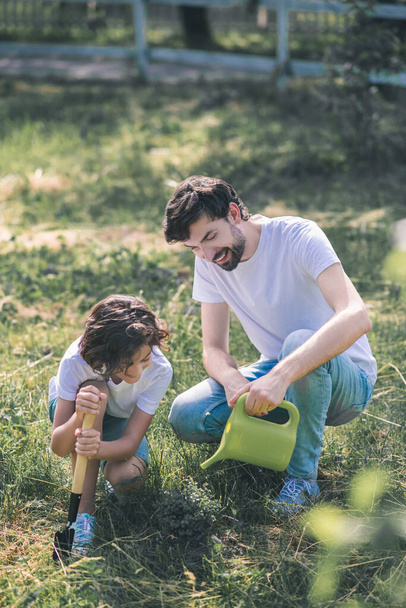 Dark-haired man watering the plant, his son watching him - Photo, image