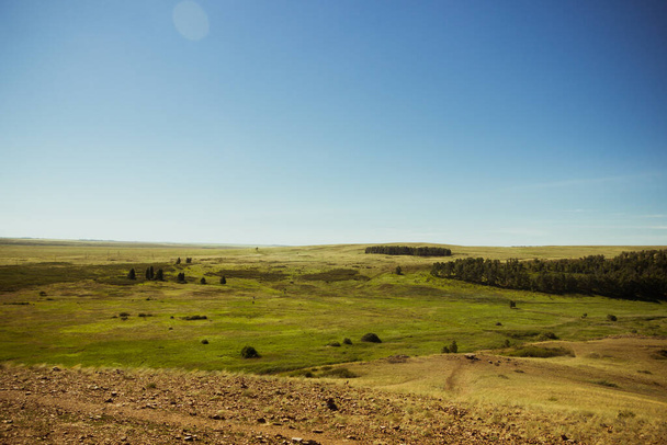 Steppe in the summer. A beautiful bottom view of the sandy steppe hills covered with green grass and wildflowers against the backdrop of a clear blue sky. Arkaim reserve. - Фото, изображение
