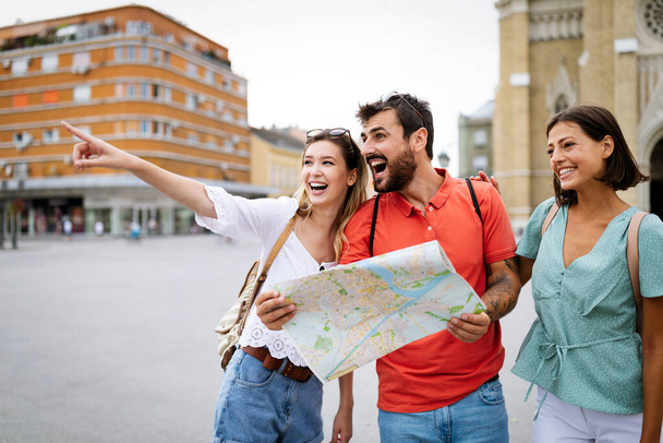 Holidays and tourism concept. Happy friends looking into tourist map in the city - Foto, Bild