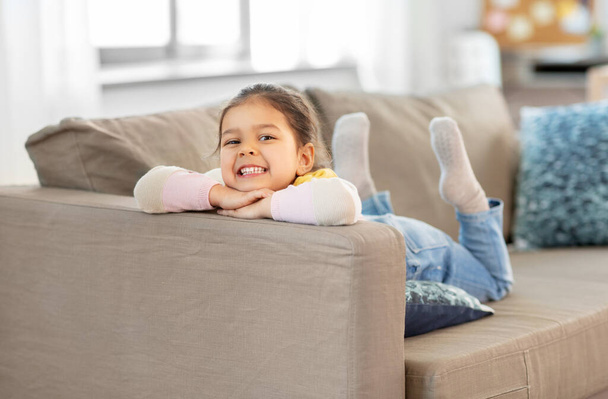 happy smiling little girl lying on sofa at home - Φωτογραφία, εικόνα
