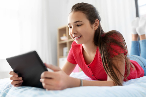 smiling girl with tablet pc lying on bed at home - Foto, Imagen